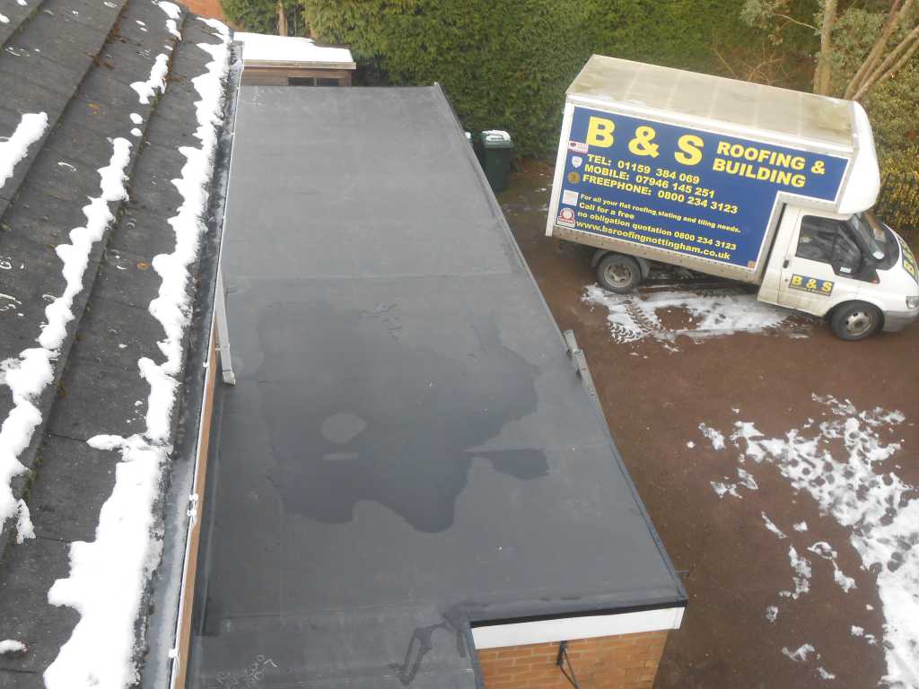 Flat Roofing with Snow on the Roof and a company van in the background to the right side